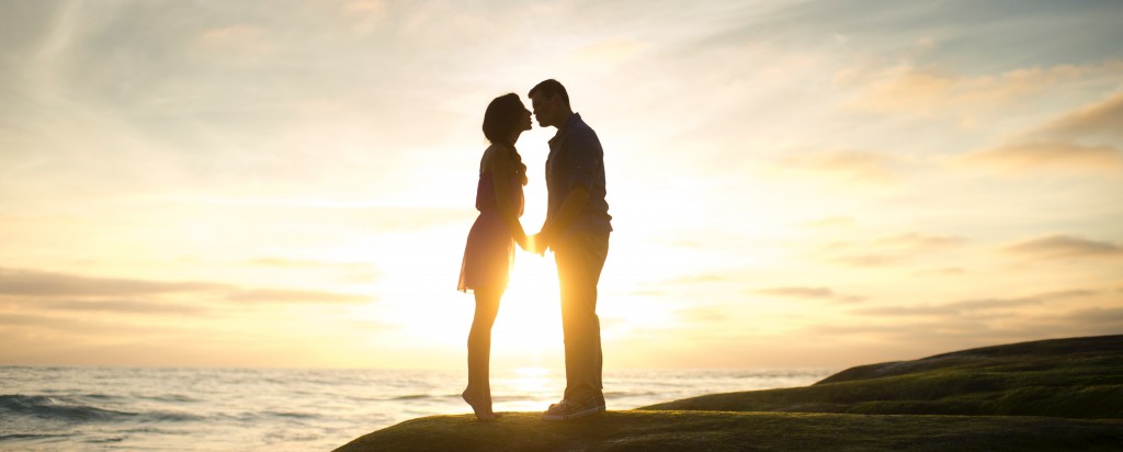 Image shows a couple kissing in front of a sunset.
